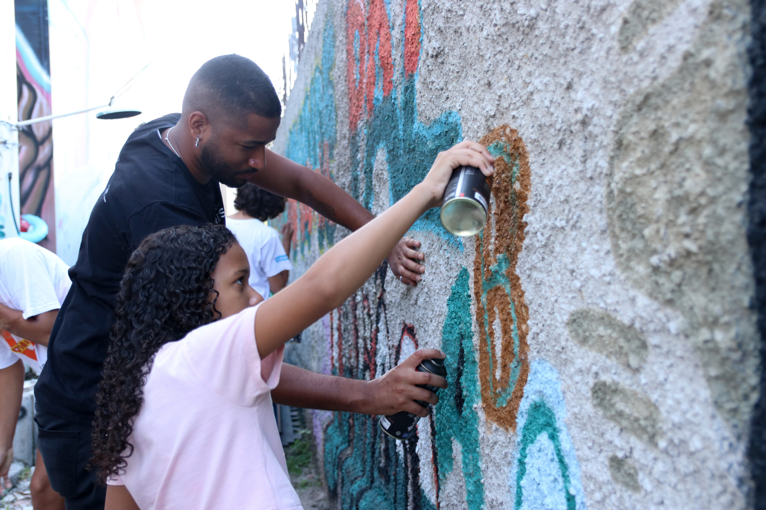 Adolescente grafitando um muro com ajuda de um professor.